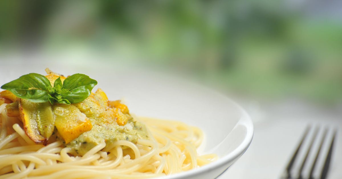 Close-up of freshly made spaghetti topped with basil and creamy pesto sauce in a white dish.