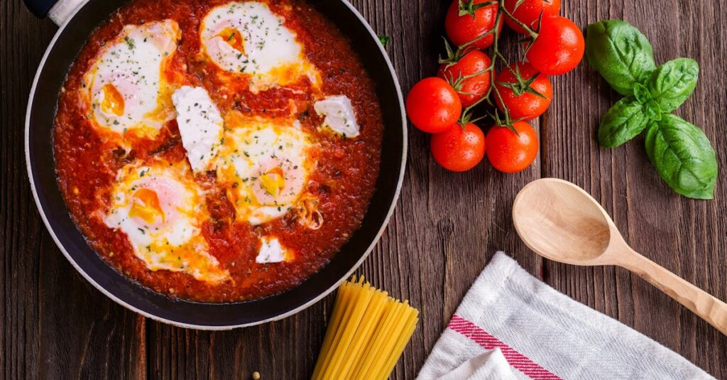 Delicious eggs in tomato sauce with basil, spaghetti, and fresh tomatoes on a wooden table.