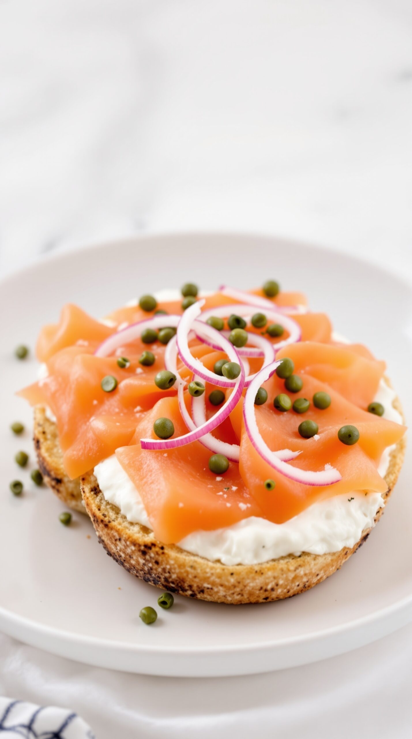 A smoked salmon bagel topped with cream cheese, red onion, and capers on a white plate.