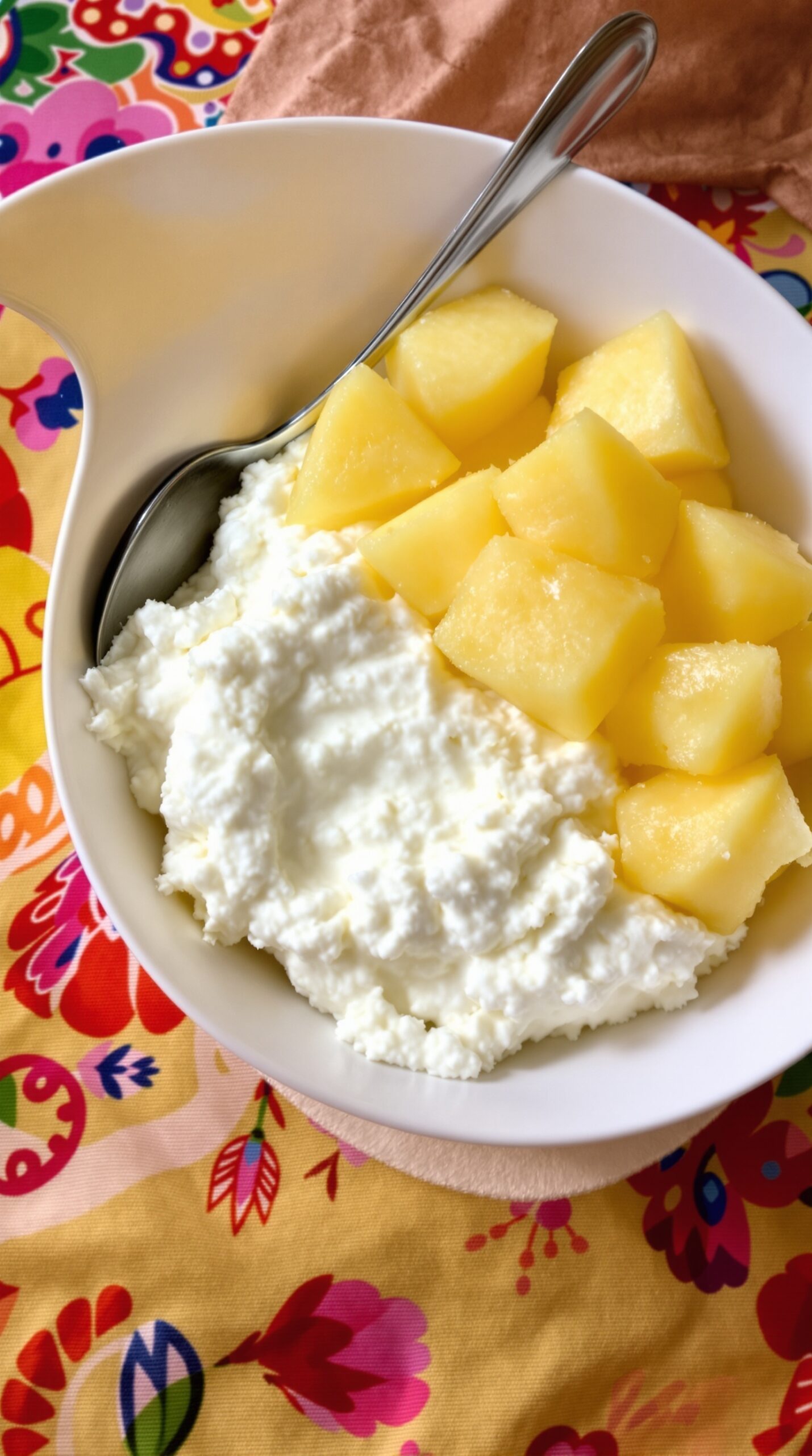 A bowl of cottage cheese topped with diced pineapple on a colorful tablecloth.