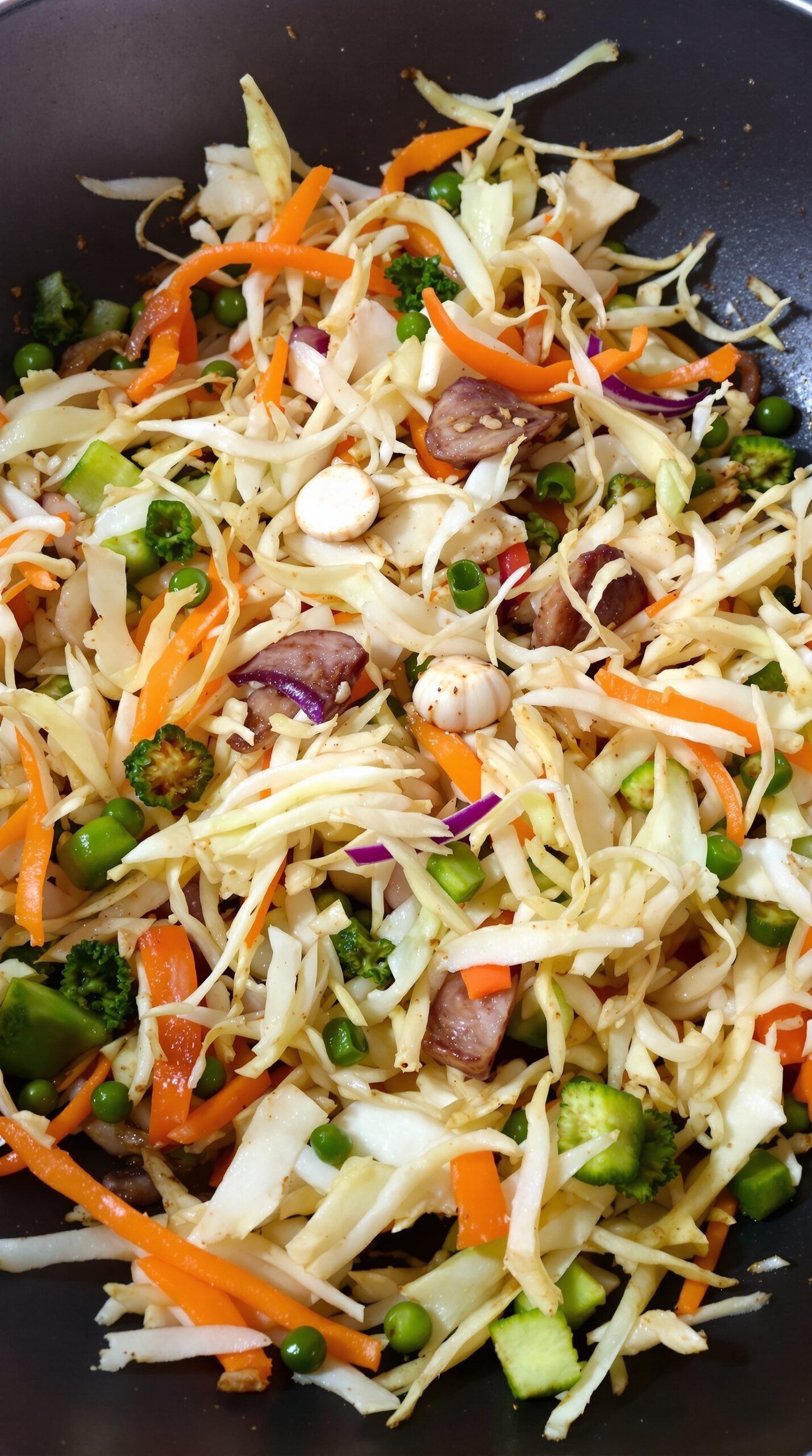 A colorful stir-fry with shredded cabbage, carrots, peas, and broccoli in a pan.
