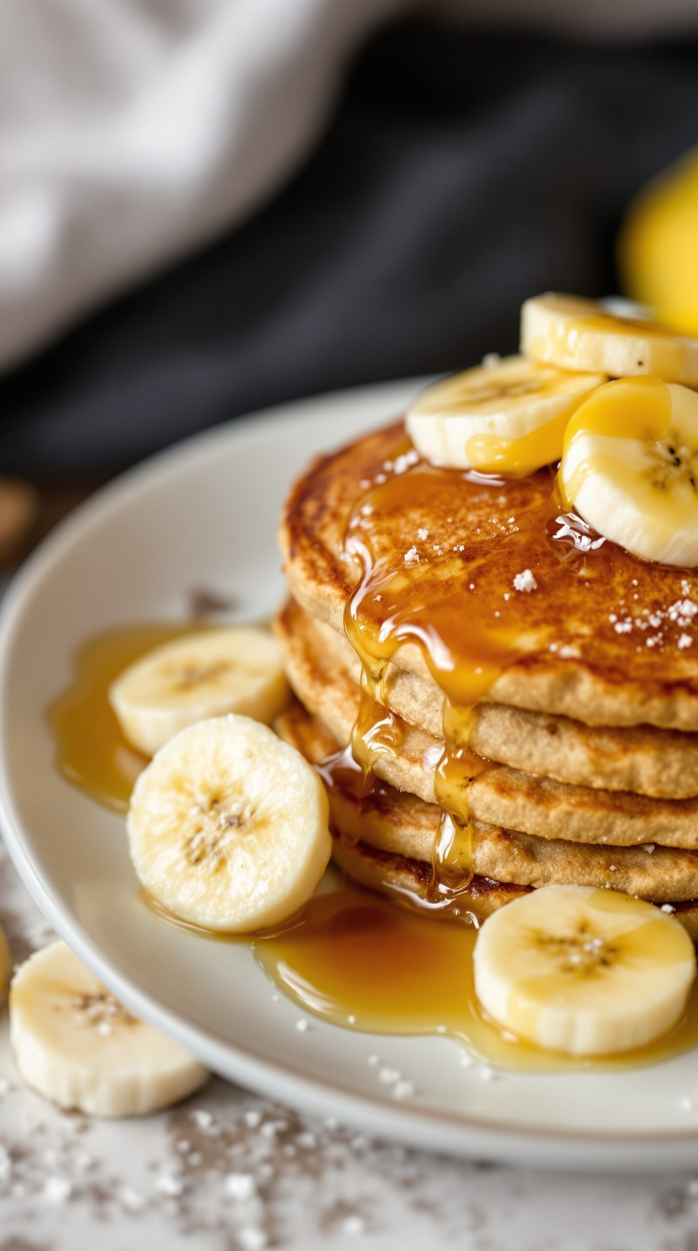 A stack of whole wheat banana pancakes topped with banana slices and syrup.